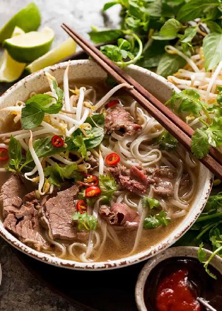 Asian soup with rice noodles and beef sprinkled with herbs and chili in a deep plate with chopsticks.