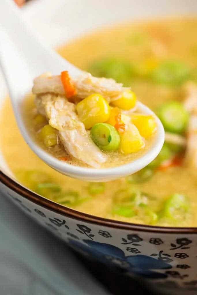 Soup with corn, chicken and spring onion, scooped with a spoon.