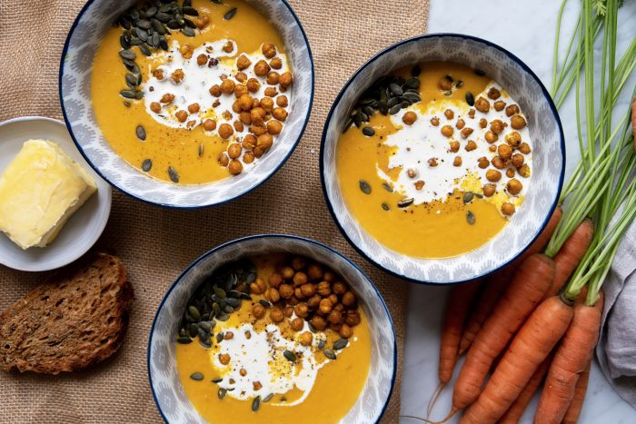 Chickpea and carrot soup served in bowls with bread and carrots on the side.