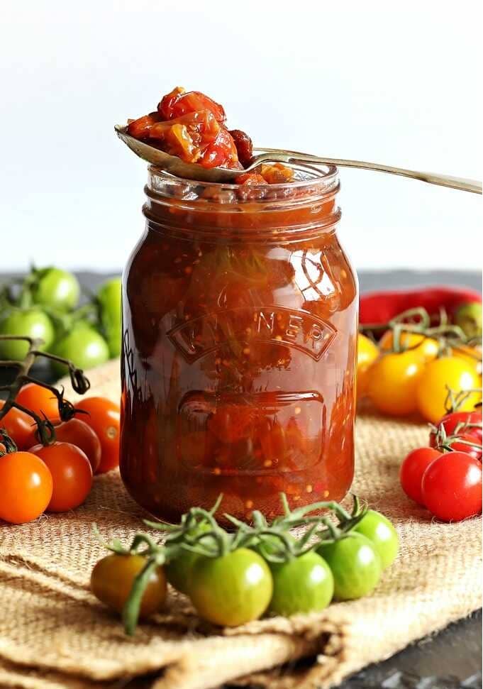 Tomato jam with horseradish in a jar with a spoon with tomatoes placed next to it.