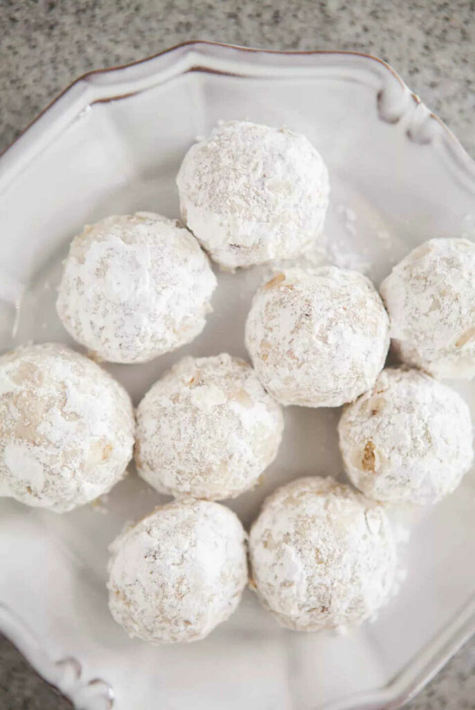 Christmas nut balls covered in powdered sugar on a decorative plate.