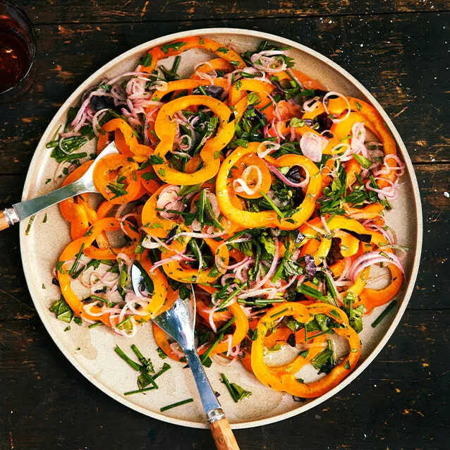 Salad with peppers and red onions served on a plate with spoons.