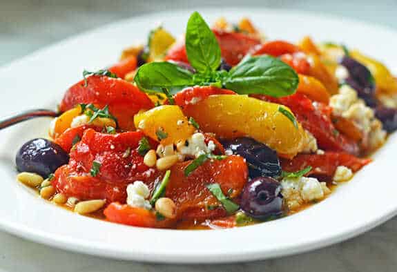 Salad with peppers, cheese, pine nuts, olives and basil on a plate.