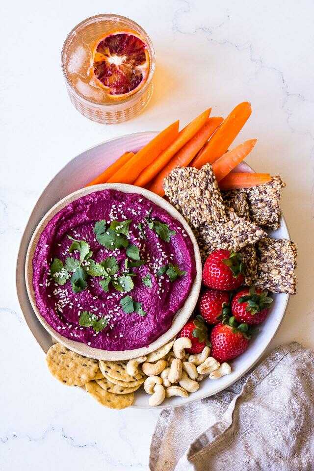 Beet spread with eggplant served in a bowl with fresh herbs, covered with carrots, strawberries, nuts and crackers.