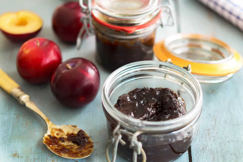 Plum jam with dates in a glass with a spoon and apples next to it.