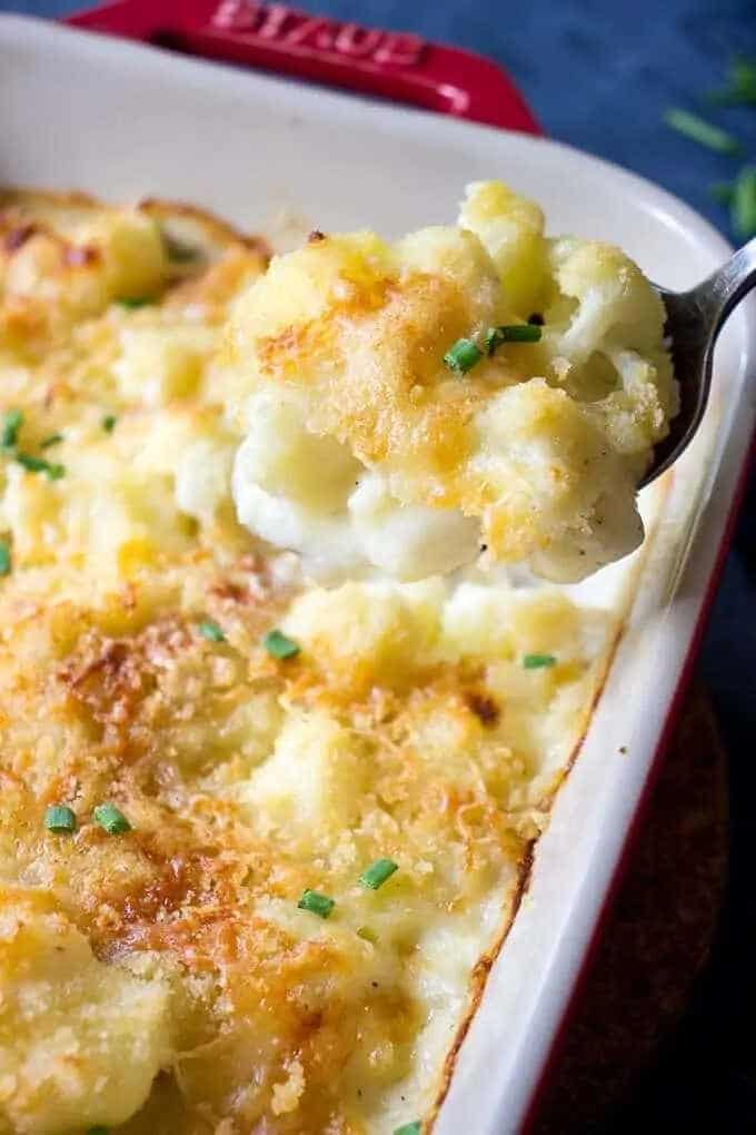 Baked potatoes with cauliflower and cheese in a baking dish scooped with a spoon.