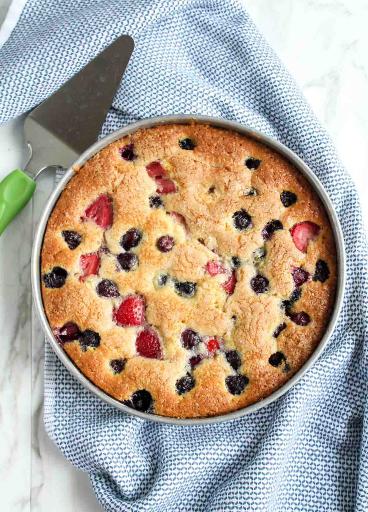 Round buttermilk cake with berries in a mold.
