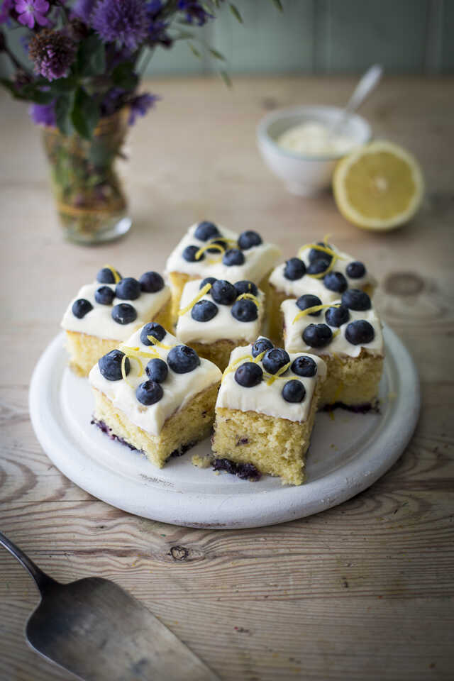 Slices decorated with mascarpone glaze, fresh blueberries and lemon zest served on a plate.