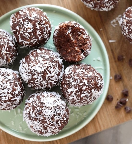 Unbaked cocoa balls coated in coconut on a plate.