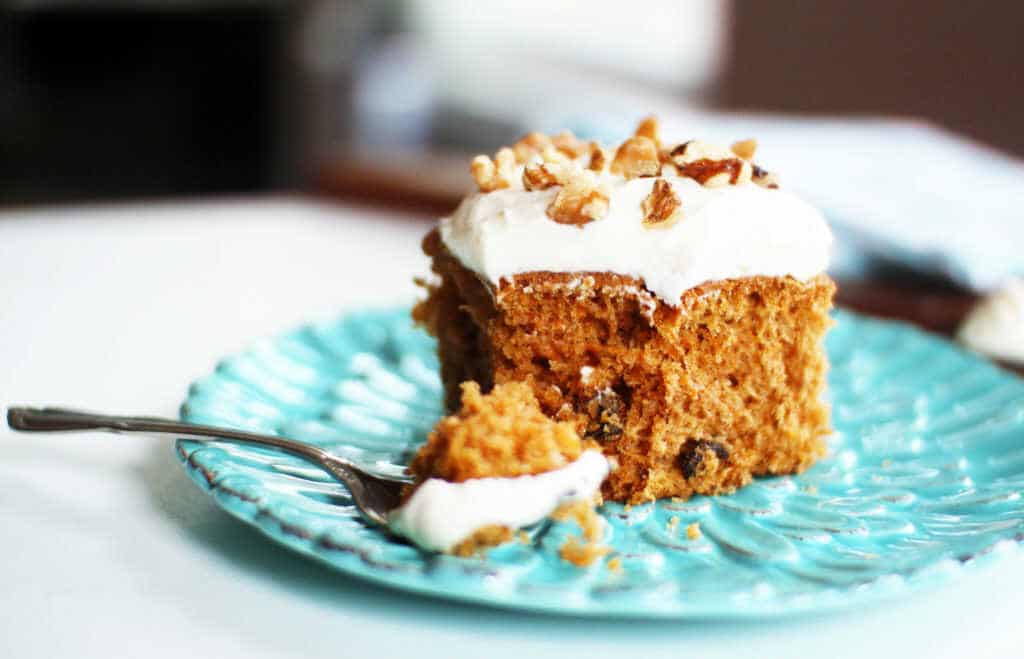 A piece of carrot bun on a plate with a fork, decorated with mascarpone and hazelnut topping.
