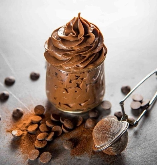 Kakaocreme in einem Glas und daneben verstreute Schokoladenstückchen.