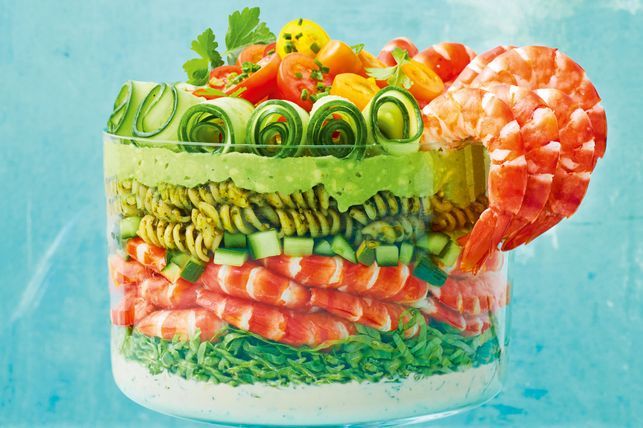 Pasta salad with pesto, vegetables and tiger prawns, served in a glass bowl.