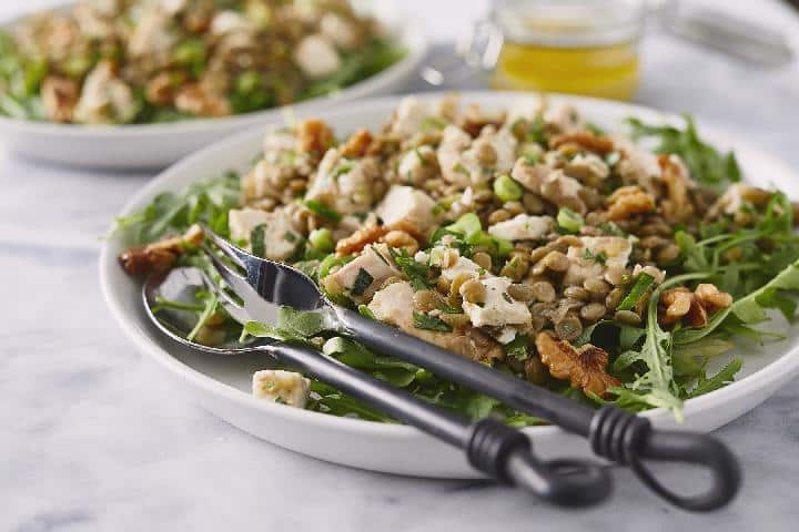 Lentil salad served on a green salad with chicken on a plate with cutlery.