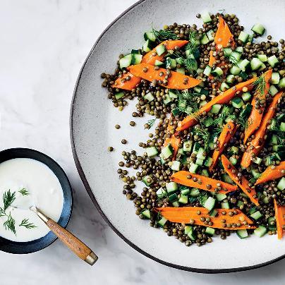 Lentils with carrots and cucumber on a plate with feta dressing on the side.