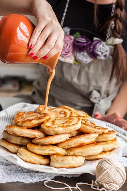 Hausgemachte Pfannkuchen aus Kefir, serviert auf einem großen Tablett, auf das eine Frau eine süße Glasur gießt.