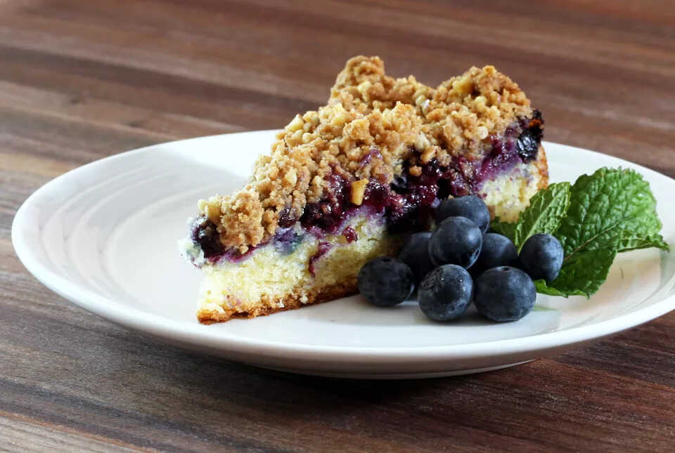 Blueberry crumb cake served on a plate with fresh blueberries and mint.