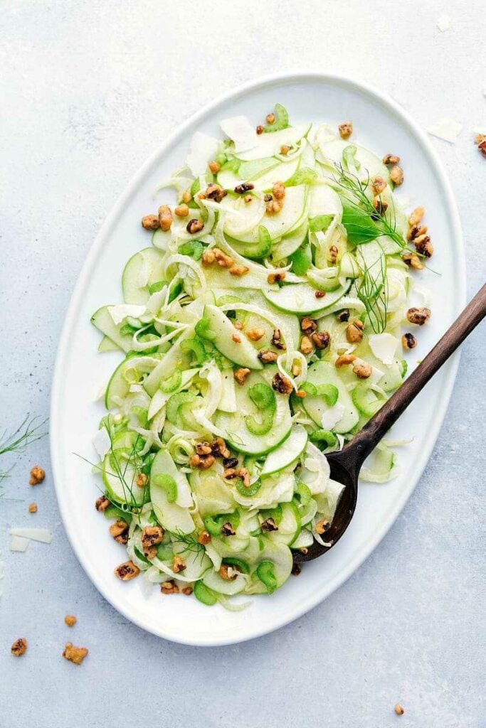Salad with green apples, fennel and nuts on an oval plate with a wooden spoon.