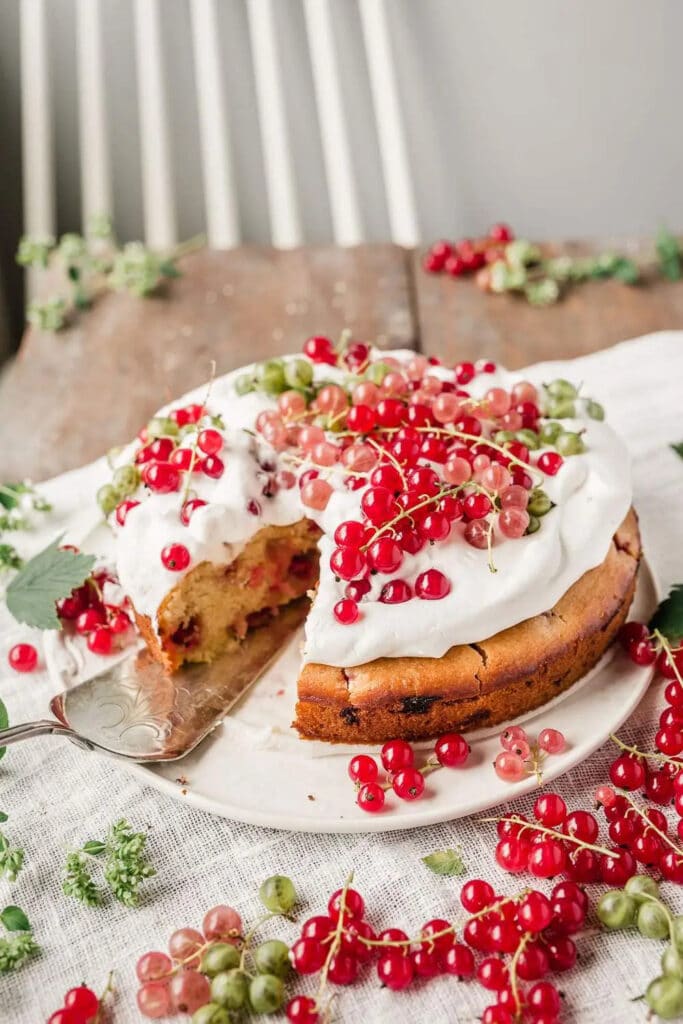 Sliced cake decorated with whipped cream and fresh red currant served on a plate.