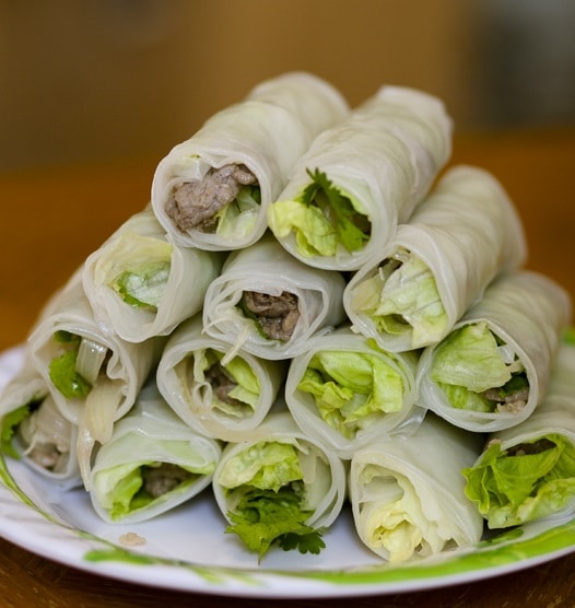 Mit Fleisch und Salat gefüllte Reisrollen, serviert auf einem übereinander gestapelten Teller.