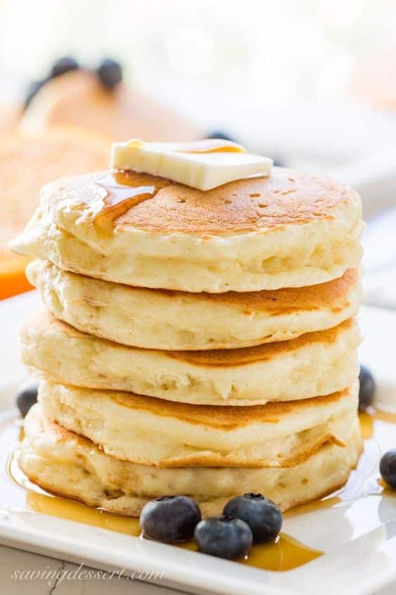A mountain of pancakes with butter and blueberries.