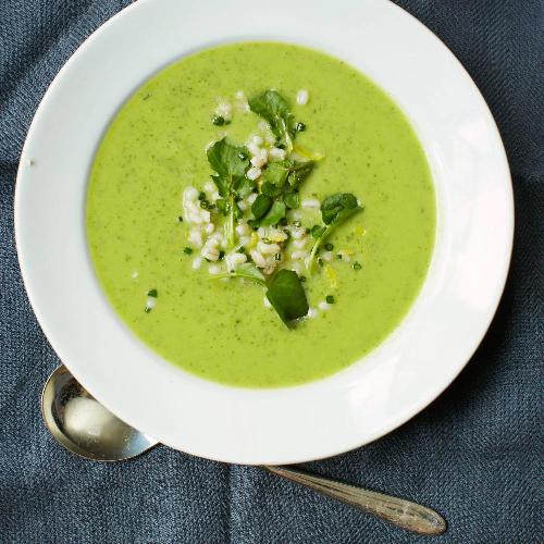 Zucchini and spinach cream with barley and watercress served in a deep plate with a spoon on the side.