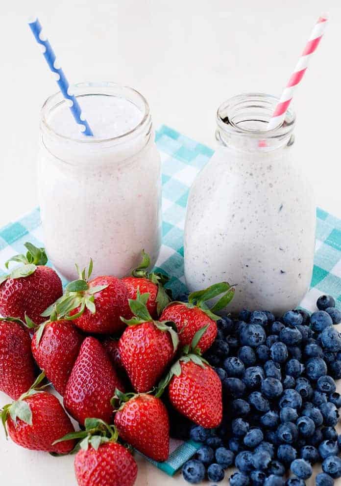Nápoj z jogurtu servírovaný ve sklenicích s brčkem, s vedle naaranžovanými jahodami a borůvkami.