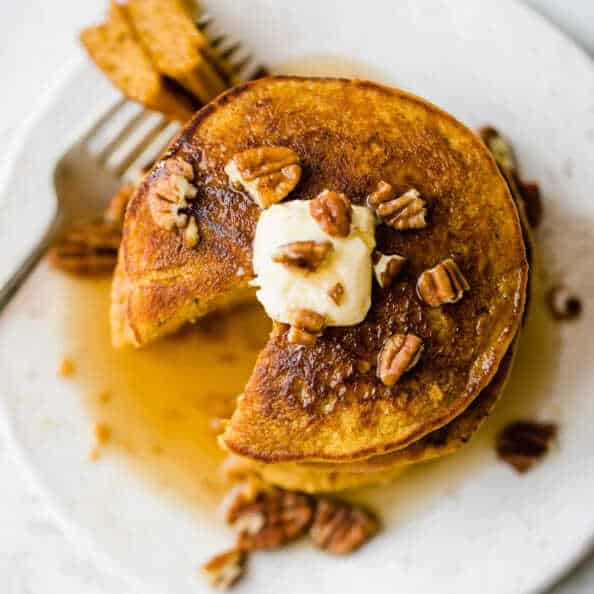 Pumpkin and oat fritters served on top of each other on a plate with a fork, covered in syrup and sprinkled with walnuts.