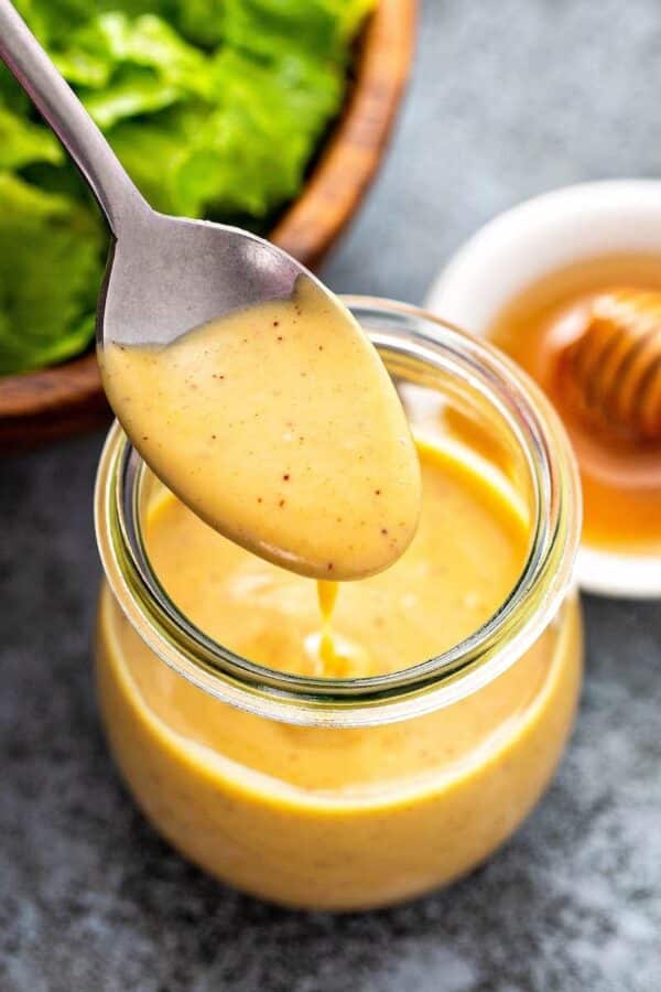 Honig-Dijon-Senf-Sauce, serviert in einem Glas und mit einem Löffel aufgeschöpft.