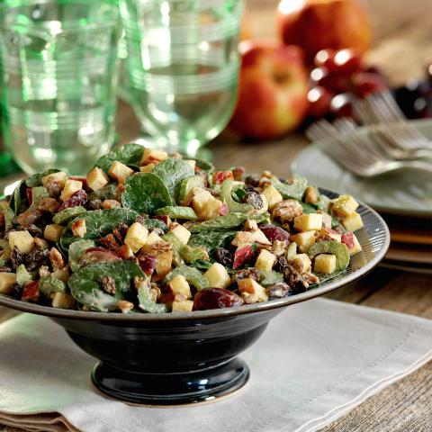 A salad of crisp apples, juicy grapes, sweet raisins, walnuts, tender baby spinach and a light dressing on a decorative plate.