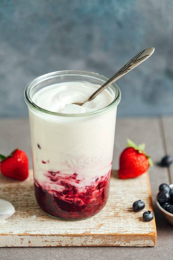 Vegetable yogurt from coconut milk served in a glass with fruit and a spoon.