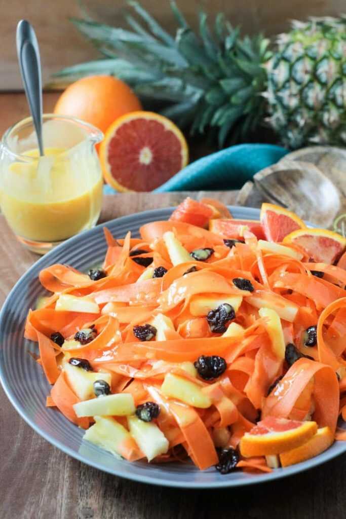 Karotten-Ananas-Salat serviert auf einem Teller mit einem Glas Dressing daneben.