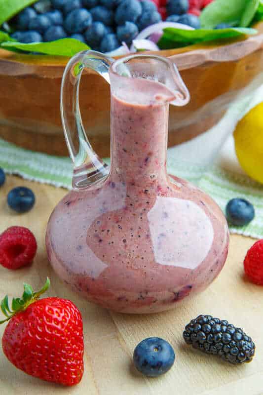 Dresink z řeckého jogurtu, lesního ovoce, máku a bílého balzamiku ve skleněné láhvi s vedle položeným ovocem.