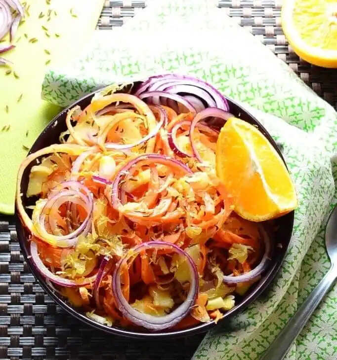 Carrot, cabbage and red onion salad, served on a plate with a lemon wedge.