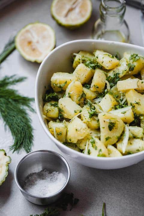 Salát z brambor a bylinek servírovaný v misce s vedle položenou mističkou se solí.