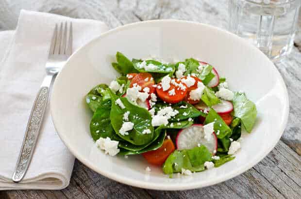 Salad with tomatoes, radishes and goat cheese served on a plate with a fork placed next to it.