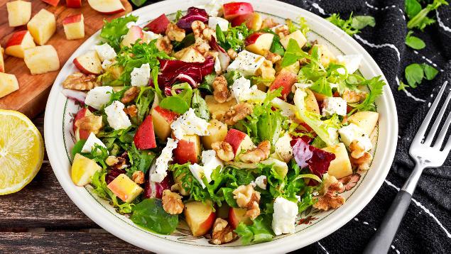Salad with fruit, lettuce and nuts with a spicy creamy blue cheese dressing served on a large plate with a fork placed next to it.