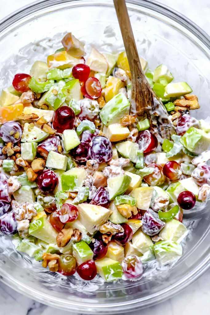 Salad with crisp apples, celery stalks and toasted walnuts with dressing served in a salad bowl.