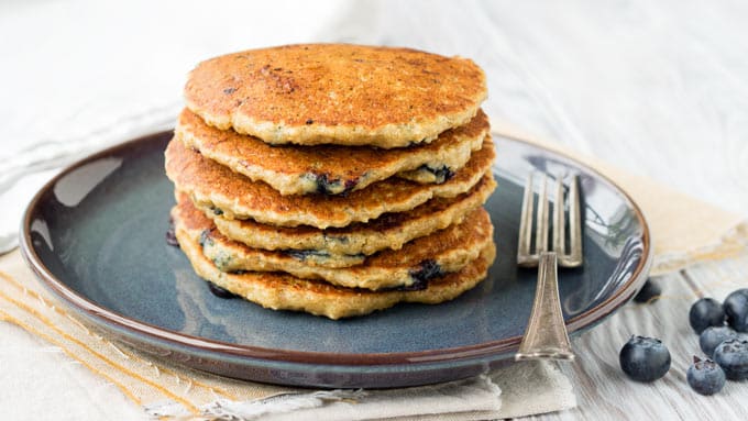 Blueberry-oat pancakes served on top of each other on a plate with a fork.
