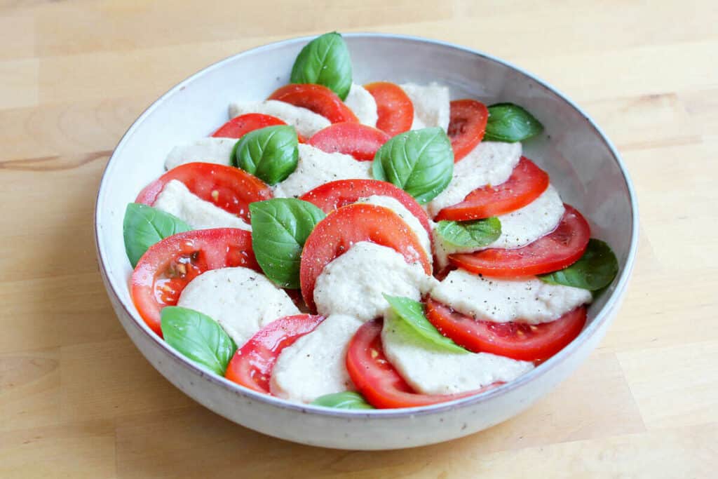 Salat mit veganem Mozzarella, Tomaten und Basilikum in einer Schüssel.