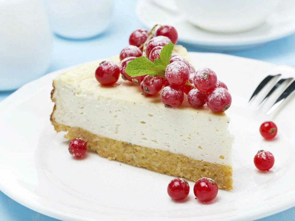 A piece of cheesecake decorated with currants, served on a plate with a fork.