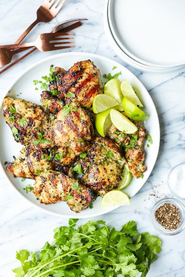 Marinated chicken quarters served on a plate, sprinkled with cilantro and with citrus wedges.