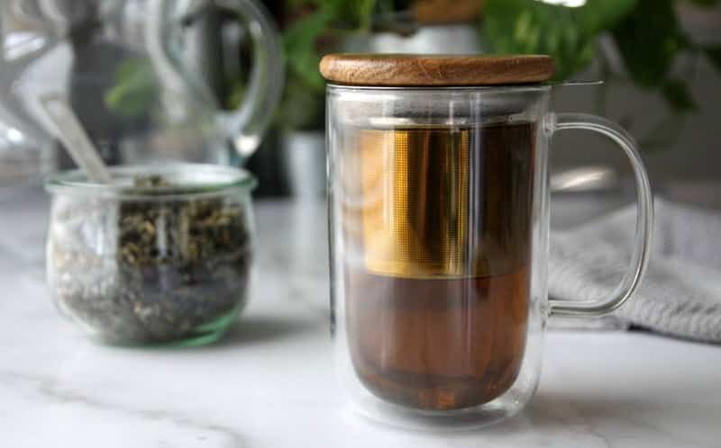 Maliníkový čaj ve skleněném hrníčku s vedle položenou sušenou směsí.