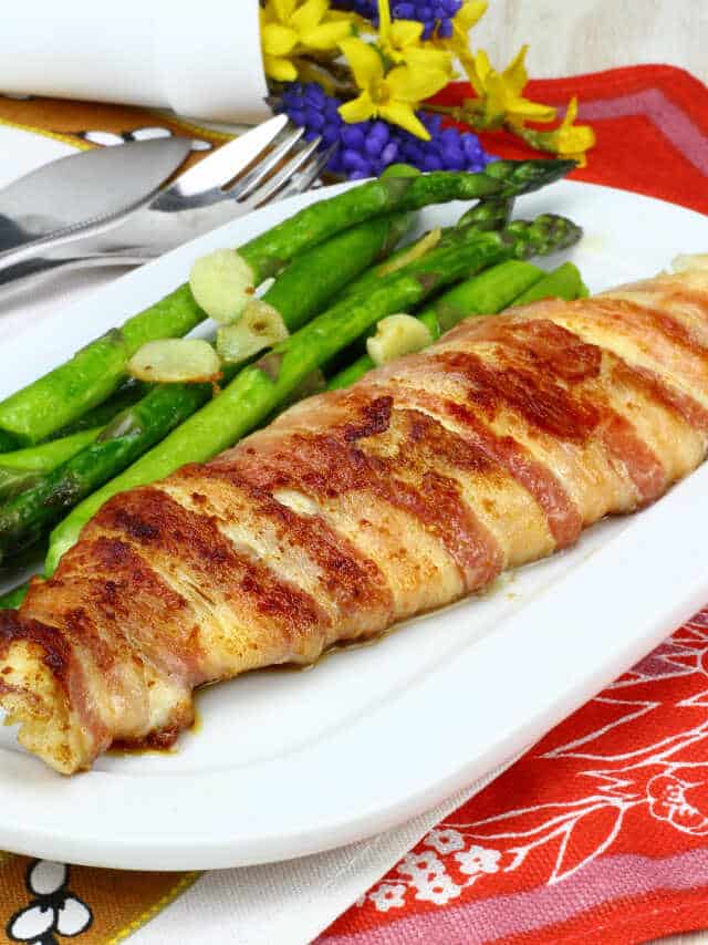 Fish wrapped in bacon, served with asparagus and garlic cloves.