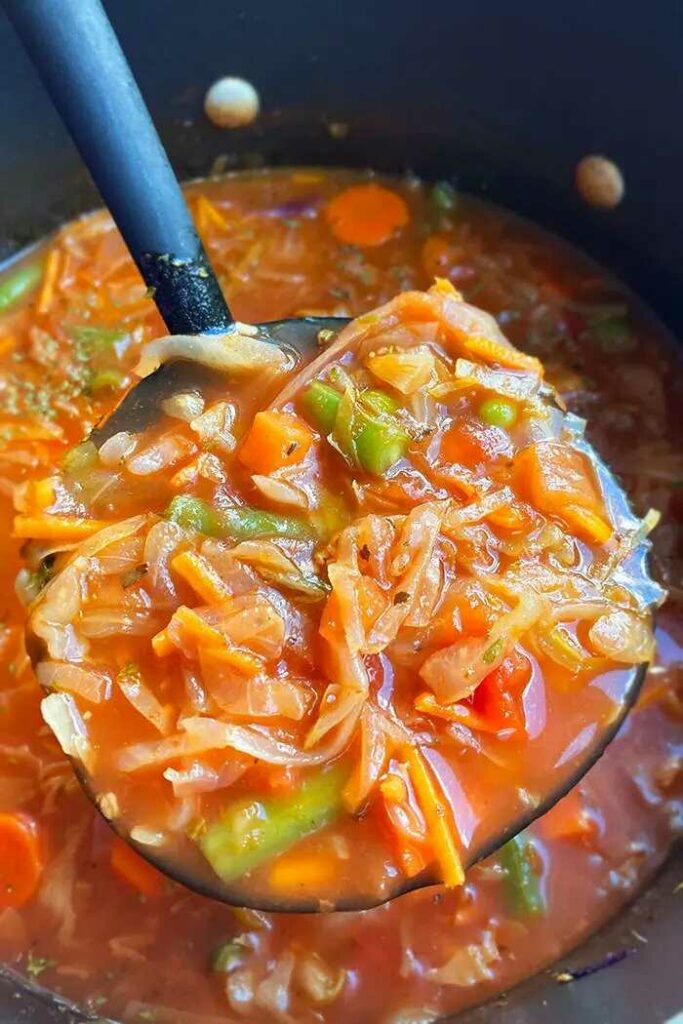 Suppe aus Kohl und anderem Gemüse, die mit einer Kelle aus dem Topf geschöpft werden.