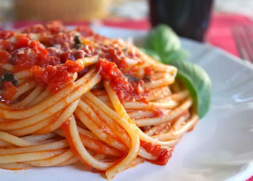 Špagety s rajčatovou omáčkou servírované na talíři s lístky bazalky.