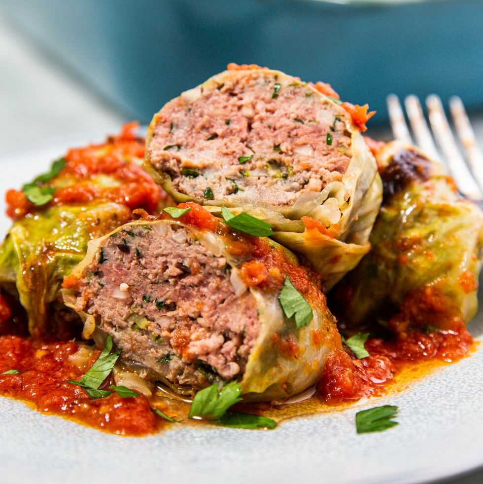 Rolls made of cabbage leaves filled with minced meat, served on a plate and covered with tomato sauce.