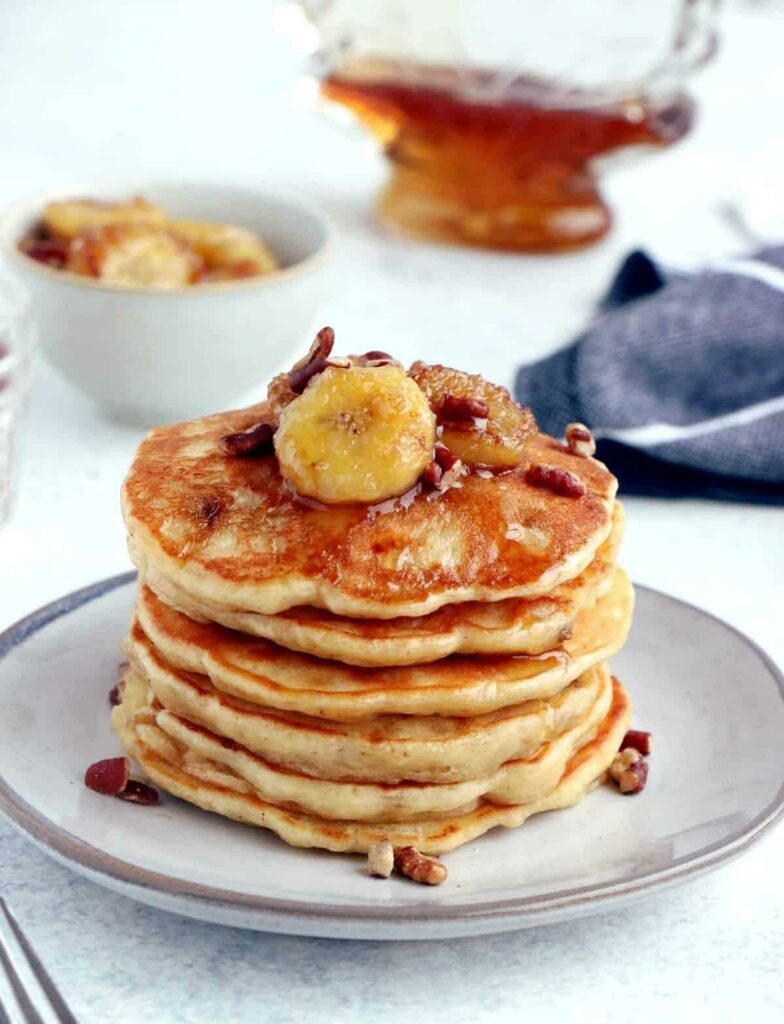 Pancakes with bananas stacked on a plate, covered in maple syrup.