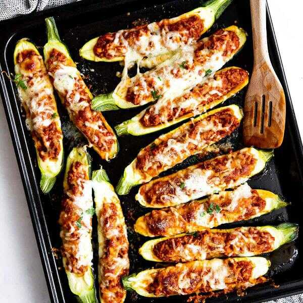 Zucchini baked with minced meat, tomato sauce and cheese on a baking sheet with a wooden spoon.