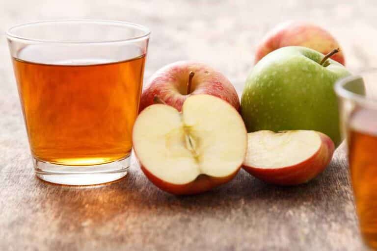 Džus z jablek nalitý ve sklenici, která je položena vedle čerstvých jablek.
