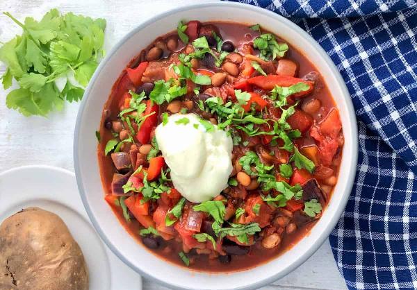 Bean and vegetable stew served in a deep plate, garnished with sour cream and fresh herbs.